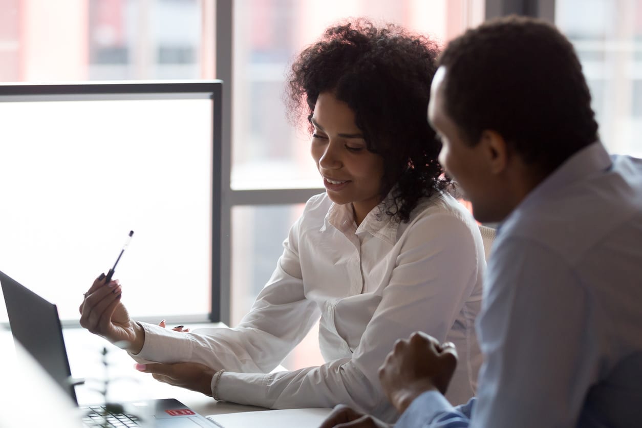 Black business partners sitting at desk looking at computer screen Mixed race pretty millennial businesswoman sitting together with african american business partner, smart people negotiating using computer looking at device screen cogitating making decision concept