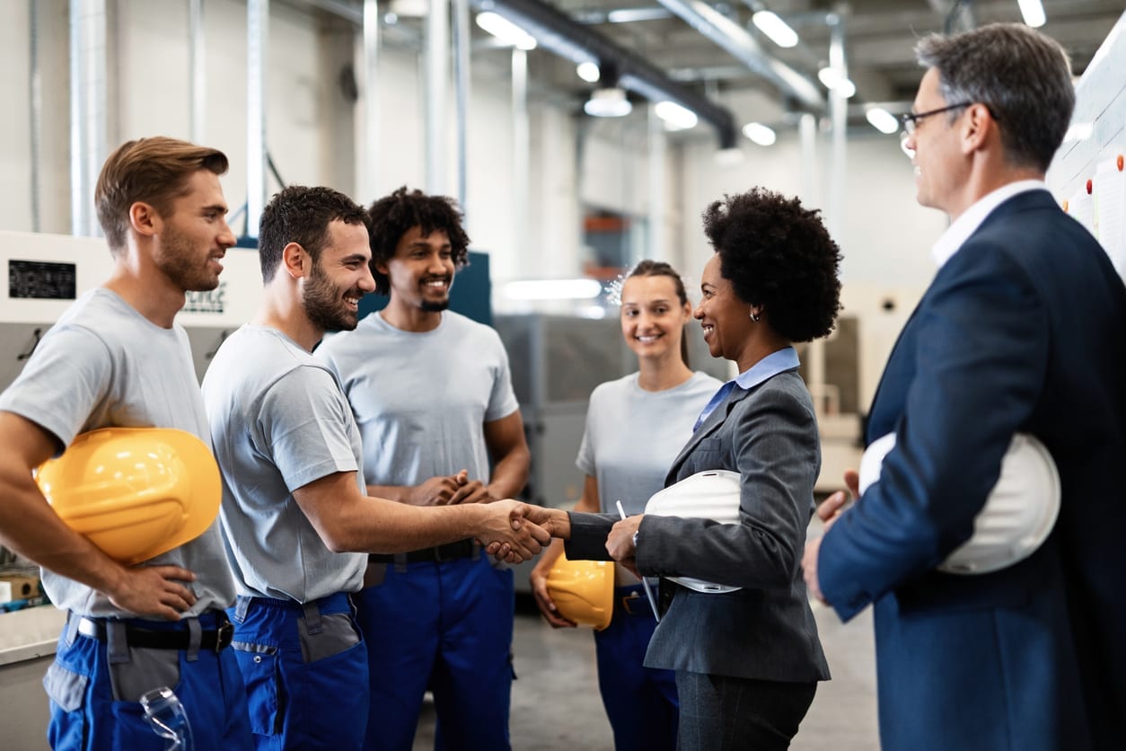 Happy African American businesswoman shaking hands with one of factory workers. Happy manual worker handshaking with African American manager who is visiting factory with her colleague.