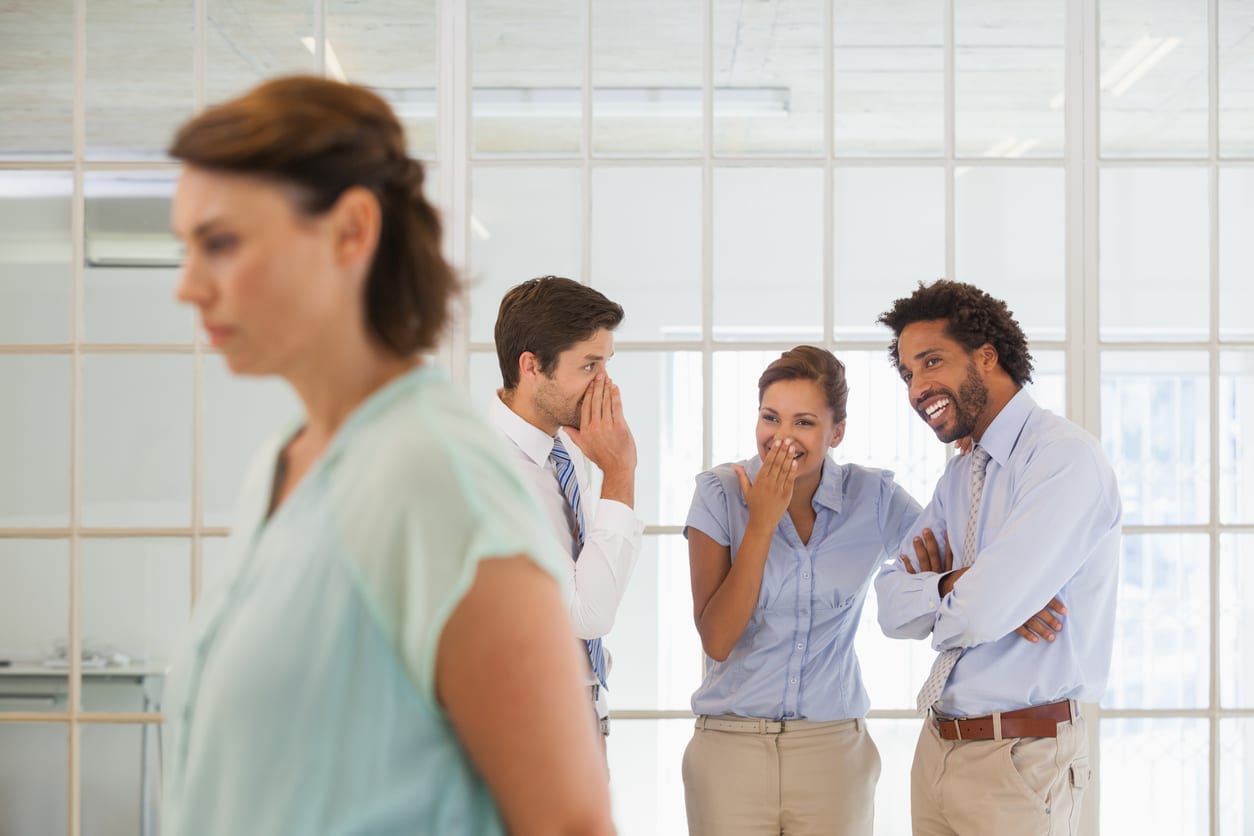 Colleagues gossiping with sad businesswoman in foreground Colleagues gossiping with sad young businesswoman in foreground at a bright office